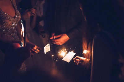 Midsection of people holding illuminated sparklers at night