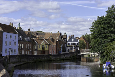 Bridge over river by buildings against sky