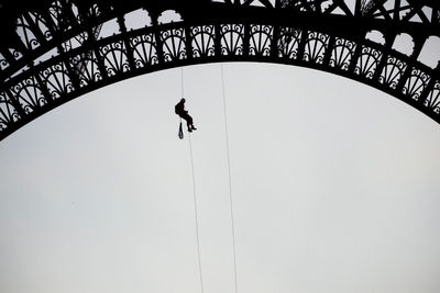 Low angle view of worker hanging on eiffel tower against clear sky