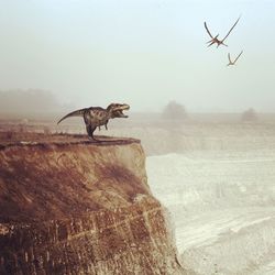 Digital composite of dinosaur and birds over rocky landscape