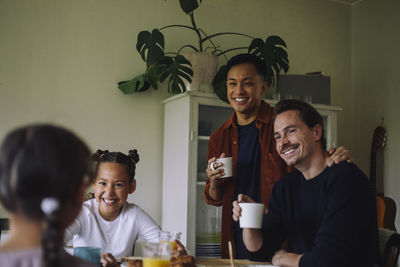 Happy gay couple talking with daughters while having breakfast at home