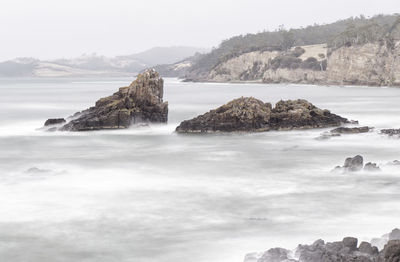 Muted colour long exposure image of sea and rocks against sky