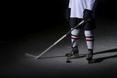 Low section of man playing ice hockey against black background