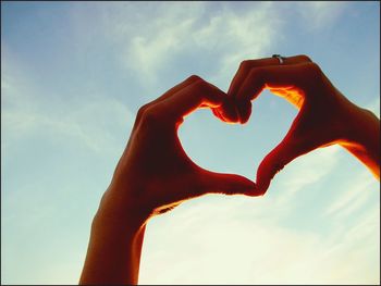 Low angle view of hand holding heart shape against sky