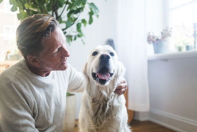 Retired man embracing while looking at dog in living room