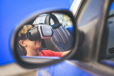 Boy wearing virtual reality simulator in car reflecting on side-view mirror