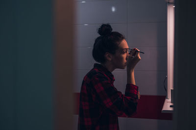 Side view of young woman applying make-up