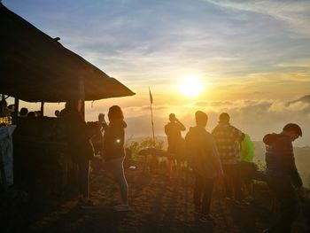 People standing on shore against sky during sunset