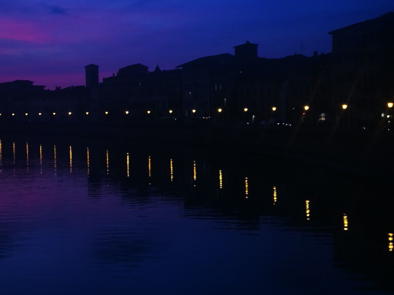 ILLUMINATED BUILDINGS BY RIVER AT SUNSET