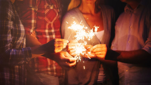 Midsection of woman holding sparkler at night