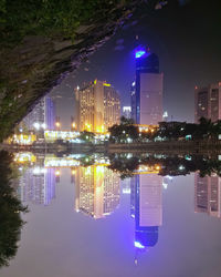 Illuminated modern buildings by lake against sky in city at night