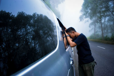 Man standing by car against trees