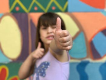 Portrait of girl showing thumbs up while standing against wall