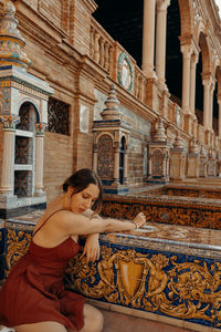 Portrait of young woman sitting in front of historic building