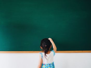 Rear view of girl writing on blackboard in classroom