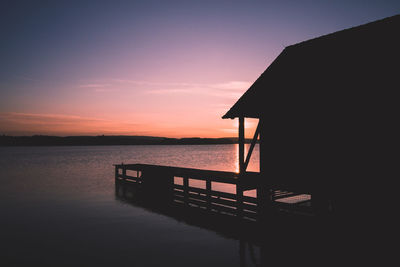 Silhouette built structure by sea against sky during sunset