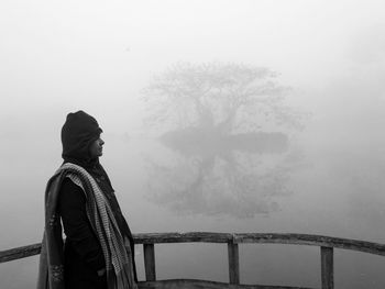 Man standing by railing on bridge against sky during winter