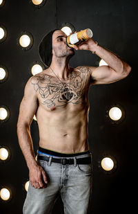 Shirtless man drinking coffee against illuminated lights