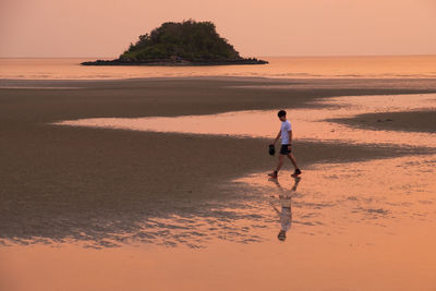 Full length of man on beach against sky during sunset