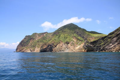 Scenic view of sea by mountain against sky