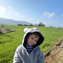 Portrait of cute smiling boy standing on field against sky
