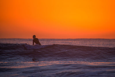 Silhouette surfer surfing in sea against sky during sunset