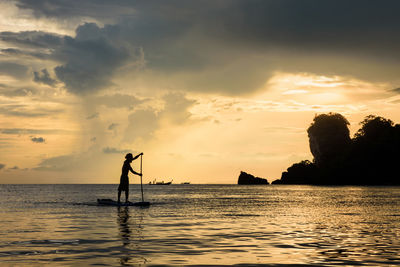 Silhouette man paddleboarding in sea against sky during sunset