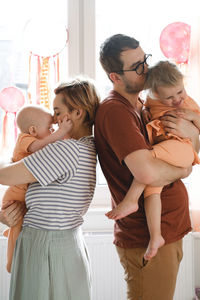 Mother and father hugging children over decorated with dreamcatchers sunny window at home. happy