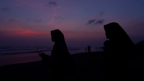 Silhouette people on beach against sky during sunset