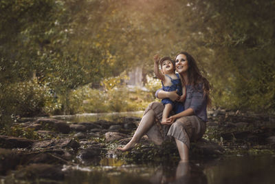 Full length of a smiling young woman sitting in forest