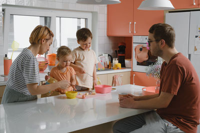 Happy family with kids cooking on modern kitchen. children cutting fruit salad, preparing food with