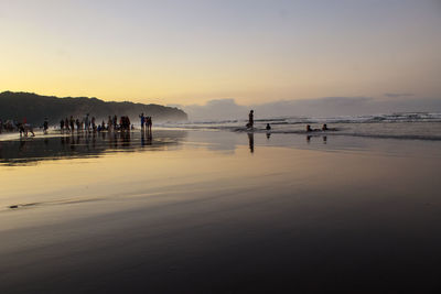 Silhouette people on beach against sky during sunset