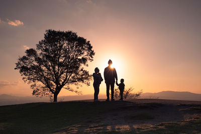 Silhouette people standing on land against sky during sunset