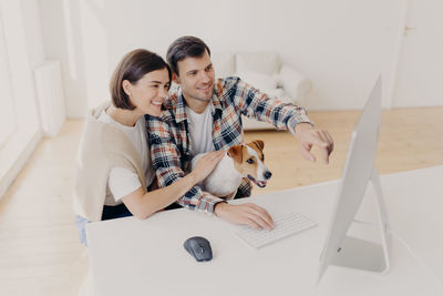 High angle view of smiling couple with dog using computer on table at home