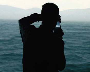 Rear view of silhouette man photographing sea