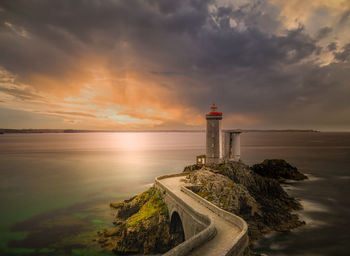 Lighthouse by sea against sky during sunset