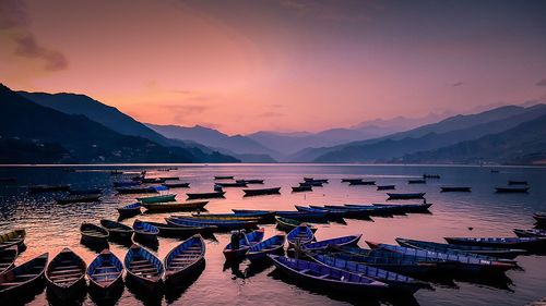 Rowboats moored in lake against sky during sunset