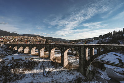 Bridge over snow covered mountains against sky