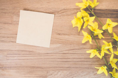 Blank adhesive note by yellow flowers on table