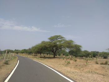 Road by trees on field against sky