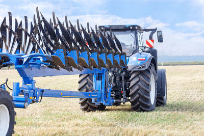 A metal multirow plow is attached to a tractor standing on an agricultural field.