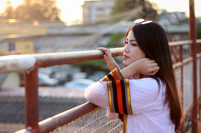 Side view of thoughtful woman standing by fence