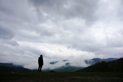 Silhouette man standing on landscape against clouds
