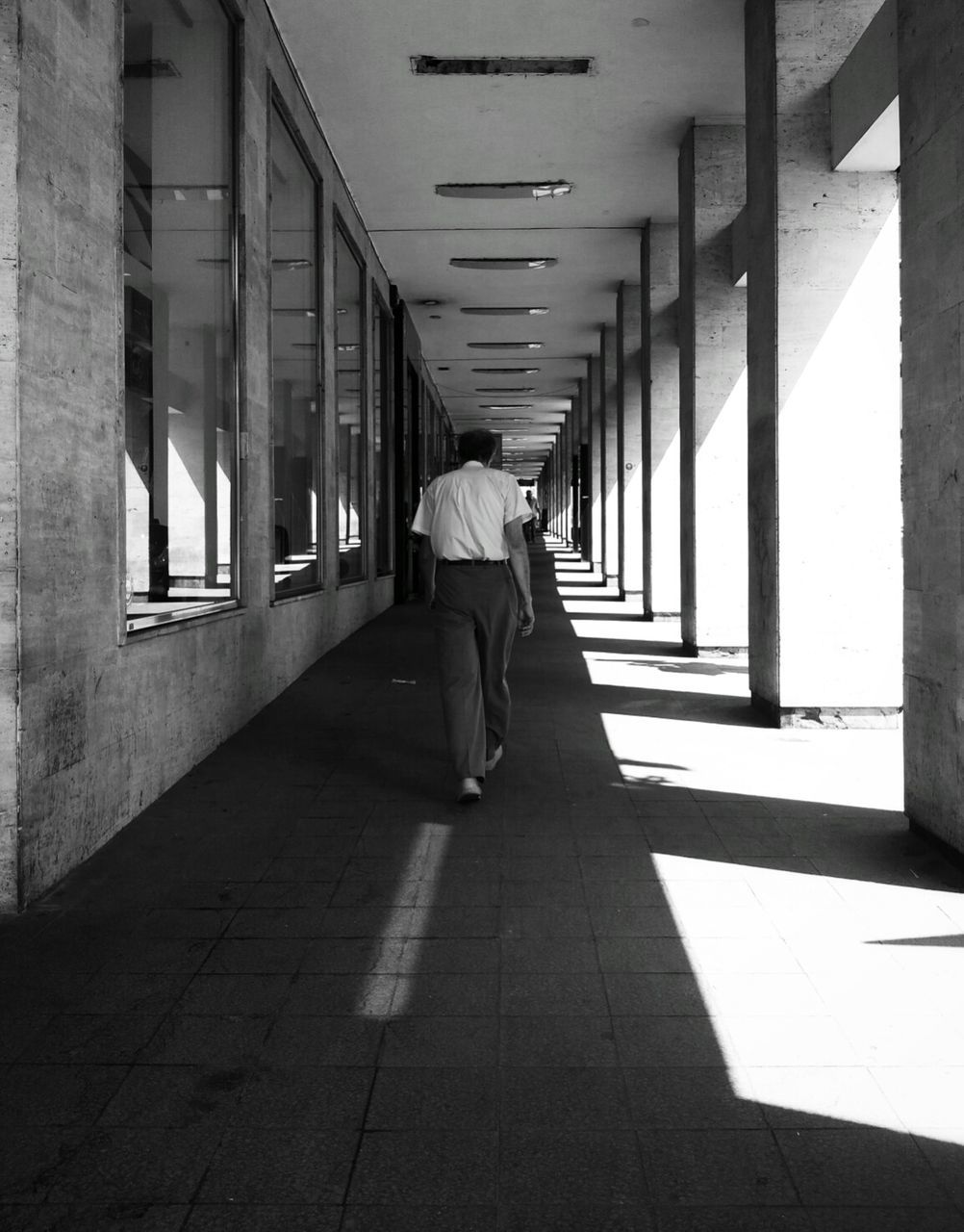 indoors, full length, lifestyles, architecture, built structure, walking, corridor, rear view, leisure activity, person, the way forward, men, flooring, tiled floor, city life, building, reflection, day