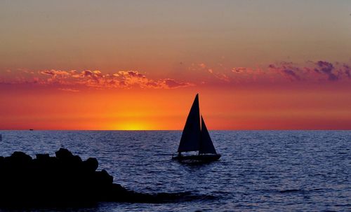 Sailboat sailing in sea against sky during sunset