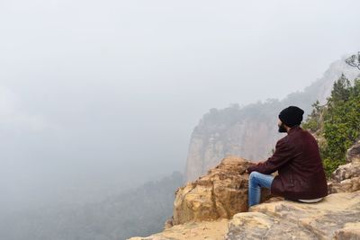 Rear view of man sitting on rock looking at mountains