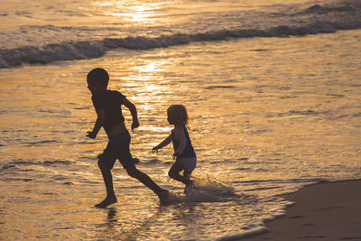 Children playing on sand at beach during sunset
