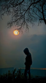 Rear view of woman standing on field against sky during sunset