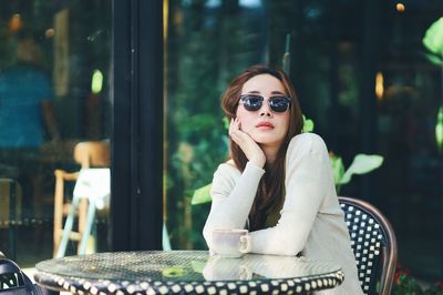 Portrait of young woman wearing sunglasses while sitting outdoors