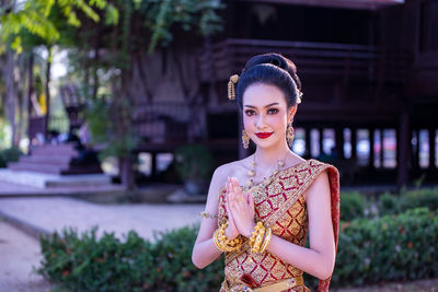 Portrait of beautiful young woman in traditional clothing standing with hands clasped outdoors